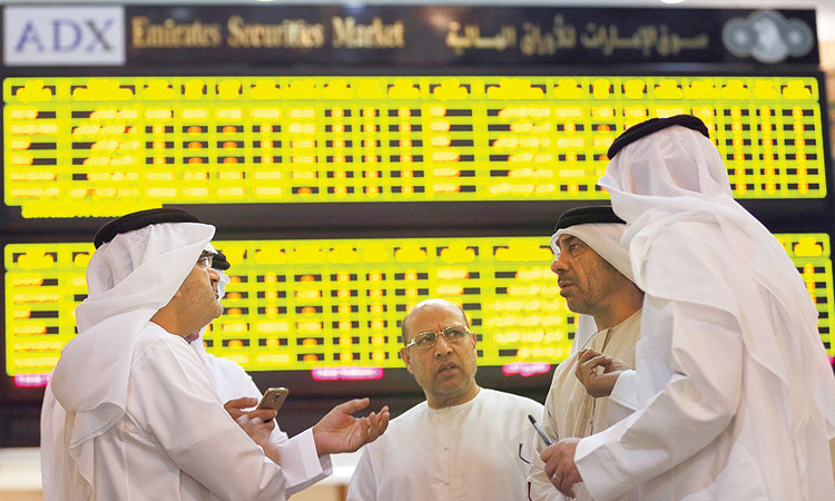 Investors speak in front of a screen displaying stock information at the Abu Dhabi Securities Exchange.