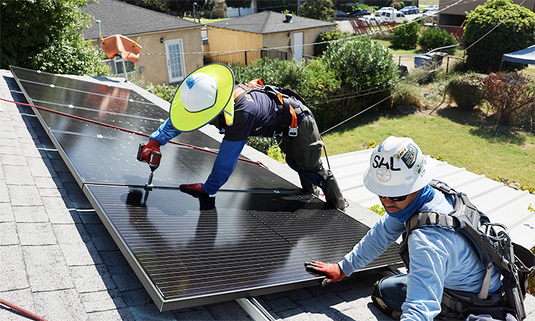 Workers install solar panels on the rooftop of a house.
